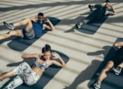Thumbnail 4 of 4 - Three people are exercising on black mats in a sunlit room.