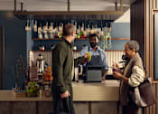 Thumbnail 20 of 24 - A man in a green sweater is standing at a bar with a bartender.