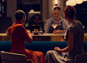 Thumbnail 19 of 24 - A woman in a red dress is sitting at a bar with a bartender.