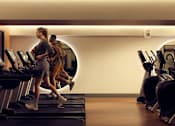 Thumbnail 21 of 24 - A woman is running on a treadmill in a gym.