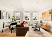 Thumbnail 9 of 24 - A living room with a brown couch, a black coffee table, and a large painting on the wall.
