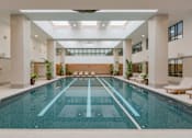 Thumbnail 6 of 24 - A large indoor swimming pool with lounge chairs and plants.