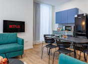 Thumbnail 15 of 27 - a living room with a table and chairs and a kitchen with blue cabinets
