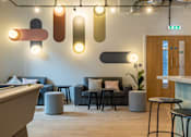 Thumbnail 12 of 27 - a lobby with couches and stools and a bar and lights on the ceiling