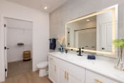Thumbnail 31 of 38 - a bathroom with white cabinets and backlit mirror on the wall