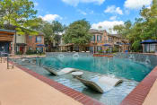 Thumbnail 34 of 40 - a swimming pool with two lounge chairs in front of a building at Aston at Cinco Ranch, Katy, 77450