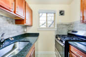 Thumbnail 2 of 22 - kitchen with wood cabinetry, gas range, tile backsplash, and window at cambridge square apartments in bethesda md
