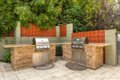Thumbnail 30 of 40 - Apartments For Rent In Encino CA - White Oak Terrace - Exterior View Of Community Barbecue Grills Featuring Two Stainless Steel Built-In Grills on Rough Stone Outdoor Kitchen Counters