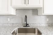 Thumbnail 11 of 22 - a sink in a kitchen with white tile and a black faucet