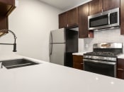 Thumbnail 4 of 23 - White tiled kitchen with modern faucet, stainless steel appliances, and refrigerator.
