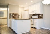 Thumbnail 24 of 29 - View of kitchen with wood look flooring, stainless appliances, tile backsplash, and white cabinets