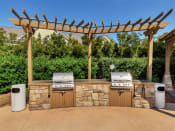 Thumbnail 21 of 61 - A large stone grilling station with two outdoor grills under a wooden pergola near trees