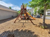 Thumbnail 36 of 61 - Rope hanging from the playground on a floor of wood chips  near a bench, street parking, and trees
