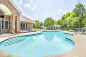 Thumbnail 4 of 25 - Leasing Office Exterior with Swimming Pool and Sun Deck with Lounge Chairs Near Tree-line
