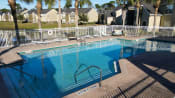 Thumbnail 9 of 15 - Community pool with sundeck, lounge chairs, with lake view surrounded by white metal fence with palm trees and building exteriors in the background
