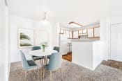 Thumbnail 18 of 25 - Model Apartment with Dinette Table in Front of Framed Wall Art Next to Open Kitchen with White Cabinets with Wood Accents and White Appliances