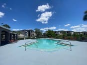 Thumbnail 1 of 31 - Community pool with sundeck, lounge chairs, surrounded by black metal fence with trees, lake, and building exteriors in the background