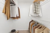 Thumbnail 29 of 30 - a walk in closet with clothes hanging on a rack and a small stool on the floor