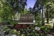 Thumbnail 1 of 18 - Park 201 Welcome Sign with Expertly Manicured Flowers and Trees at Park 210 Apartment Homes, Edmonds, Washington