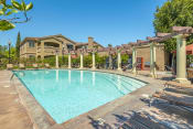 Thumbnail 5 of 13 - Elk Grove, CA Apartments for Rent- Castellino at Laguna West- Sparkling Pool with Sun Lounge Chairs and Exterior Building View