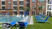 Thumbnail 1 of 40 - Heritage towers apartments an outdoor pool with lounge chairs and umbrellas in front of an apartment building lewisville tx apartments apartments near lewisville tx lewisville apartments