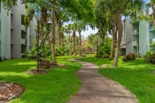 Thumbnail 6 of 30 - a path through the grass and trees in front of an apartment building