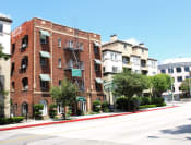 Thumbnail 26 of 28 - Street view of Brookmore apts in Pasadena CA. Four story brick building with striped awnings, fire escape, and "now leasing" sign.