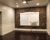 Thumbnail 9 of 28 - Living room in Brookmore apartments Pasadena CA. Large window with white blinds and trim and air conditioning unit on an exposed brick wall