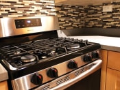 Thumbnail 10 of 28 - Apartments Pasadena - Brookmore - Kitchen With Gas Stove, Wood-Style Cabinets, and Multicolored Backsplash