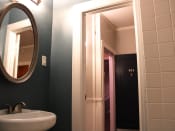 Thumbnail 14 of 28 - Bathroom in one bedroom brookmore apartment in Pasadena. Oval mirror over pedestal sink and doorway with white trim leads to hallway and front door.