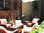 Thumbnail 16 of 28 - Brookmore Pasadena ca apartments back patio next to brick wall. Stained wood deck with cushioned wicker patio furniture and grill.