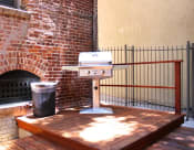 Thumbnail 17 of 28 - Brookmore Pasadena ca apartments grilling station with a stainless steel grill and trash can on a stained wood deck with railing and brick wall.