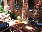 Thumbnail 15 of 28 - Brookmore Pasadena ca apartments back patio surrounded by greenery and brick wall with wicker patio furniture, stained wood deck, and grilling station.