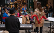 Thumbnail 17 of 24 - a woman standing in front of a crowd of musicians playing keyboards