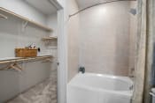 Thumbnail 14 of 34 - a bathroom with beige tiles and a white bathtub at Alta Denton Station, Denton, Texas