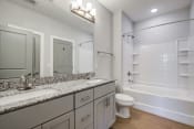 Thumbnail 42 of 48 - a bathroom with gray cabinets and a white bathtub
