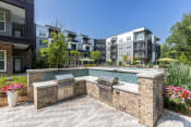 Thumbnail 3 of 32 - an outdoor kitchen with two grills next to a pool with an apartment building in the background