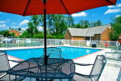 Thumbnail 32 of 36 - a swimming pool with a table and chairs under an umbrella at Chester Village Green Apartments, Virginia, 23831