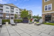 Thumbnail 15 of 29 - a large stone patio with three lounge chairs and a fire pit in front of an apartment building