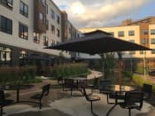 Thumbnail 4 of 52 - Outdoor seating area with umbrella and apartment building behind -Beecher Terrace Senior, Louisville, KY