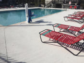 Thumbnail 18 of 24 - Row of red  chairs next to a swimming pool at River Crossing Apartments, Thunderbolt, GA, 31404