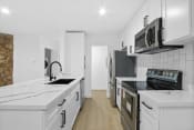 Thumbnail 1 of 12 - a kitchen with white cabinets and black appliances and white counter tops