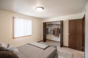 Thumbnail 5 of 16 - A bedroom with a bed and a closet with clothes in it. Bismarck, ND Eastbrook Apartments.