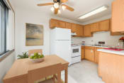 Thumbnail 4 of 8 - Bismarck, ND Riverpark Apartments a kitchen with white appliances and a wooden table with a bowl of fruit on it. The natural light from the window next to the table brightens the room