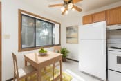 Thumbnail 3 of 8 - Bismarck, ND Riverpark Apartments a kitchen with white appliances and a wooden table with a bowl of fruit on it. The natural light from the window next to the table brightens the room