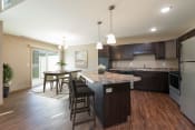 Thumbnail 4 of 11 - Bismarck, ND Stonefield Townhomes. A kitchen with dark wood cabinets and a large island with a granite countertop. The space features a well-appointed dining table, modern kitchen appliances, and tasteful decor. Bright natural light fills the room from the glass sliding door.