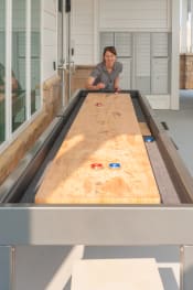 Thumbnail 15 of 17 - a woman plays a game of shuffleboard on a large shuffleboard table  at The Edison at Madison, Alabama