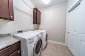 Thumbnail 16 of 22 - Laundry room with tile floors, washer and dryer, cabinets, and hanging rack.