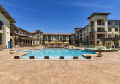 Thumbnail 18 of 38 - Apartments in Broomfield for Rent - Terracina - Outdoor Resort Style Pool With Lounge Chairs, a Fountain, and Seating Under Umbrellas