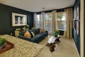 Thumbnail 2 of 48 - Pet-Friendly Apartments in San Jose, CA - Aviara - Living Room with Wall-to-Wall Carpeting, Blue Couch, Floor-to-Ceiling Windows, Glass Door to the Outside, and Wall Art